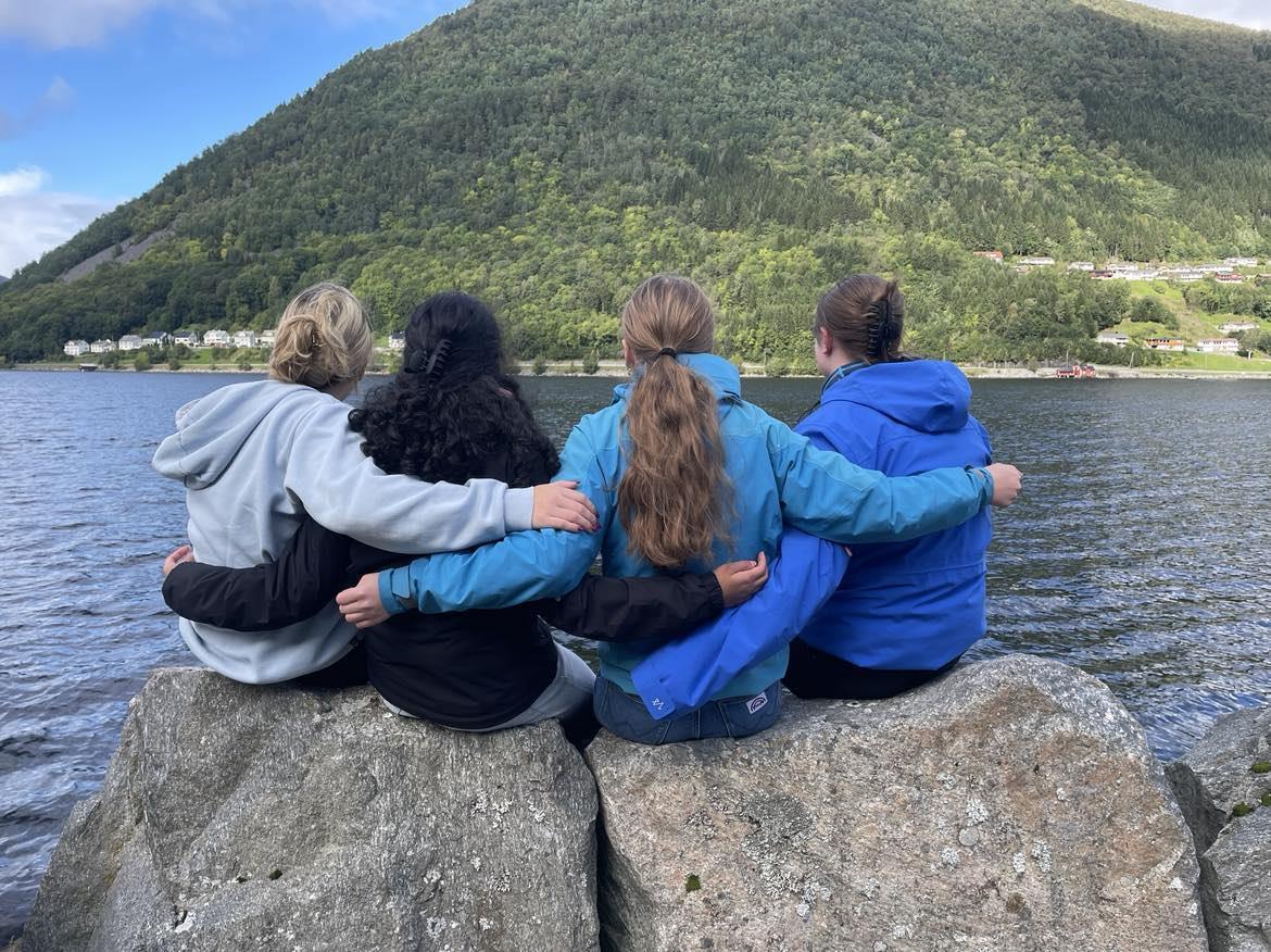 Fire jenter set med ryggen mot kamera og ser ut over sjøen - Klikk for stort bilete