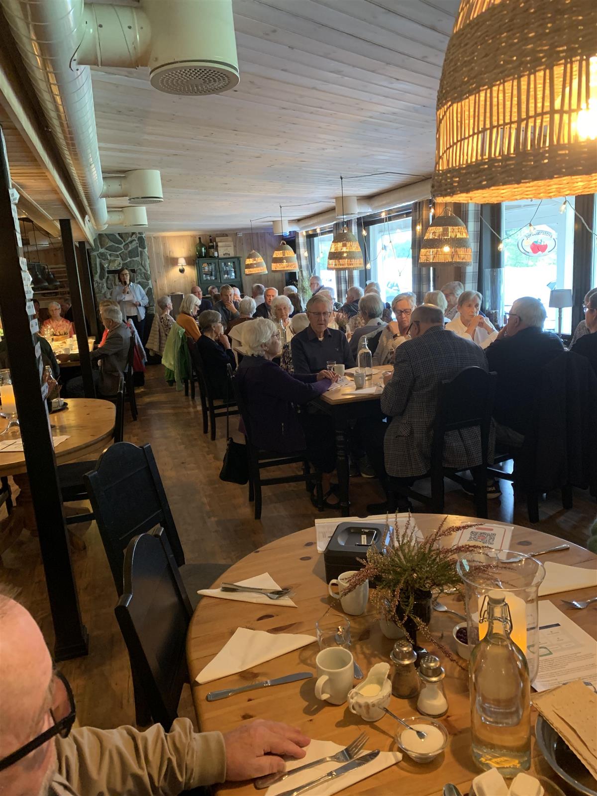 Folk samla rundt middagsbord i forsamlingslokale - Klikk for stort bilete
